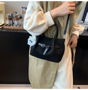 Detail view of a black woven crossbody bag with silver buckles and white plush charm