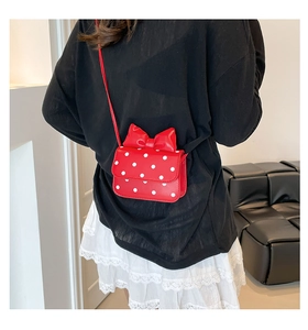 Rear view of a mini red polka dot crossbody bag with a large bow worn by a model