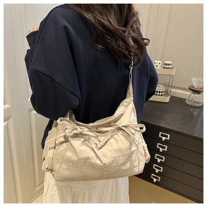 Detailed view of beige nylon cloud bag with decorative bow drawstrings worn by model