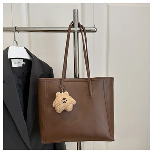 Close-up of a brown leather tote bag with fine stitching and a cute plush bear charm