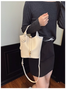 Detailed view of white lychee leather bucket bag with gold lock and smiley charm accessory