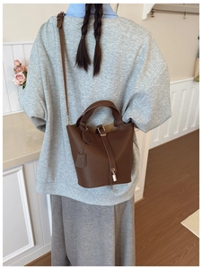 Detail of brown litchi leather bucket bag with metallic lock and round charm accessory