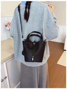 Detail of black lychee grain leather bucket bag with metal padlock and round charm