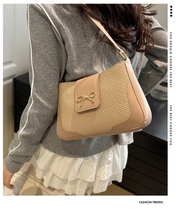 Detailed view of women's beige woven shoulder bag featuring a golden bow and slim strap