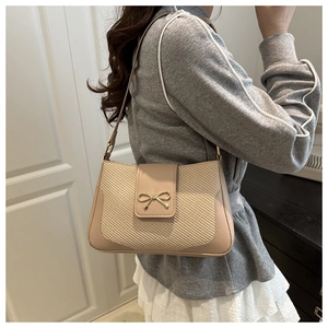 Detailed view of beige straw woven baguette bag with a golden bow buckle on a model