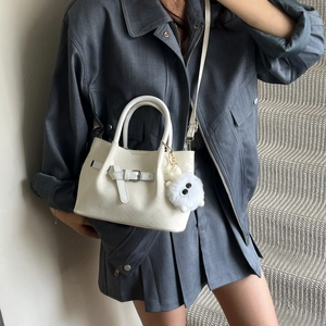 Minimalist cream woven handbag with wing accents and plush charm on a model