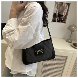 Detail of black woven PU leather shoulder bag featuring a golden metal bow fastener