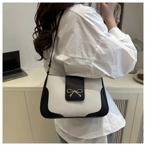 Detail of fashion crossbody bag with woven texture and gold bow metal buckle on a woman