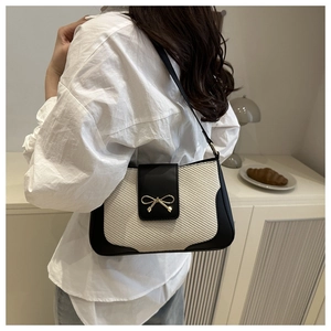 Detail of black leather and beige woven fabric shoulder bag with gold bow clasp on model