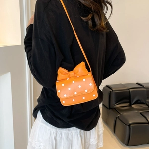 Mini orange polka dot crossbody bag with a large bow detail shown on a female model