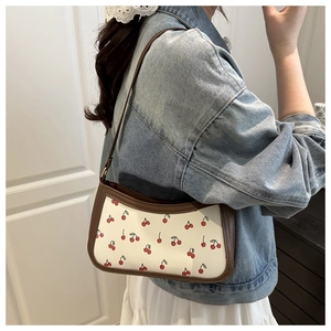 Chic underarm bag featuring red cherry print and brown leather trim on a model