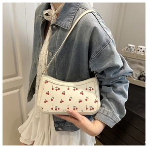 Close-up of a white cherry print shoulder bag worn with a casual denim jacket