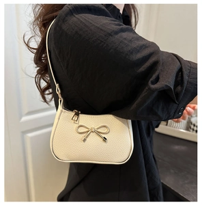 Detailed close-up of textured leather shoulder bag featuring a golden metal bow ornament