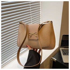 Detailed view of the fine woven texture and golden bow buckle on a beige baguette bag