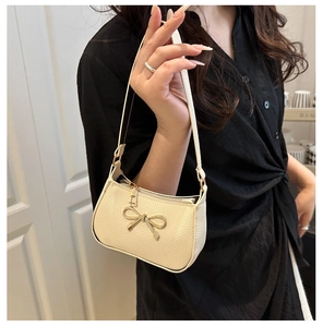 Close-up of beige lychee pattern leather bag with decorative gold metal bow detail