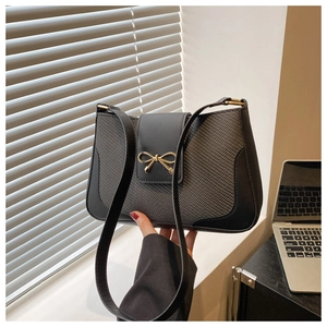 Close-up of the stylish bow buckle on a black contrast leather and woven shoulder bag