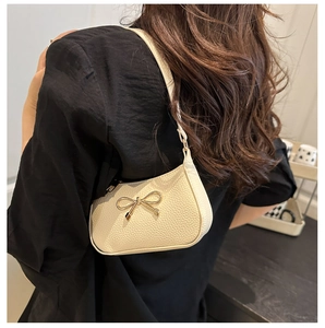 Detail of off-white lychee texture leather bag with elegant gold bow metal buckle