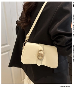 Detail of cream shoulder bag featuring an oval gold textured metal buckle and smooth leather