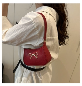 Close-up of red pebbled leather shoulder bag with gold metal bow and zipper detail