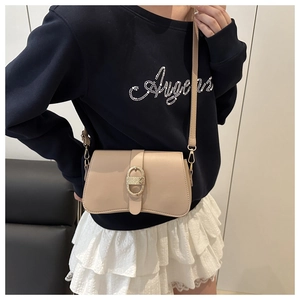 Detail of apricot faux leather crossbody bag featuring a textured gold oval buckle accent