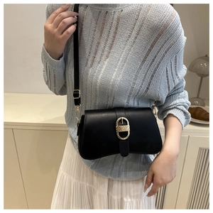 Detail of a black leather underarm bag featuring a gold oval buckle and sleek curved base