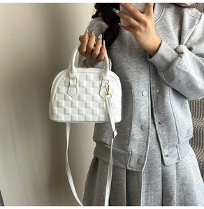 Weiße Muscheltasche mit Schachbrettmuster in der Hand zur Darstellung der Größe