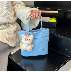 Détail du cabas en nylon bleu ciel avec breloque ours en peluche et logo embossé