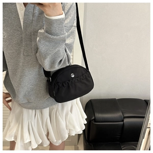 Detail of black nylon crossbody bag featuring pleated front pocket and circular metal logo
