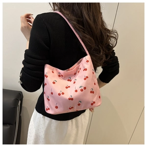 Détail d'un sac seau en nylon rose avec imprimés cerises rouges porté à l'épaule