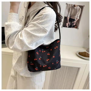 Détail d'un sac seau en nylon noir avec motifs cerises rouges porté par un mannequin