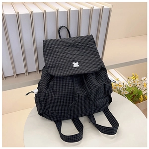 Detail view of black and white checkered drawstring backpack with puzzle piece buckle on table