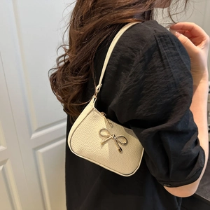 Chic beige shoulder bag with golden bow ornament shown on model in a soft indoor setting