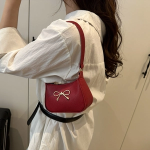 Stylish red leathery crescent underarm bag with a decorative gold bow charm