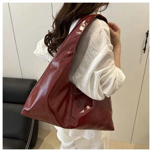Detail of burgundy high-gloss shoulder bag showing patent leather texture and carry style