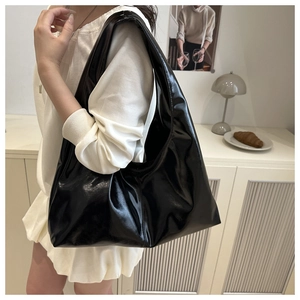 Minimalist large glossy black tote bag worn by a model in a cozy indoor setting