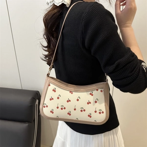Women's cream shoulder bag with red cherry print and tan leather trim on model