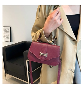 Dettaglio della borsa bordeaux in pelle martellata con chiusura dorata sulla modella