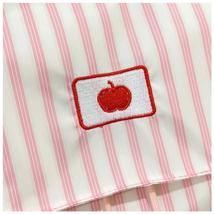 Close-up of pink and white striped fabric with a detailed red apple embroidery patch