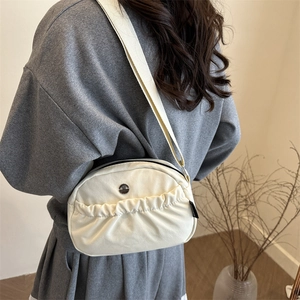 Minimalist beige nylon crossbody bag with pleated front pocket and wide shoulder strap