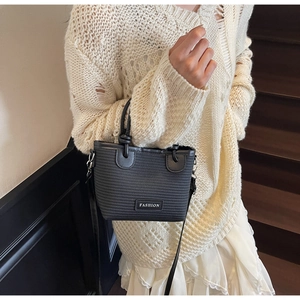 Detail of black woven crossbody bag with FASHION label on a wooden staircase