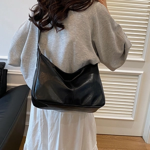 Grand sac hobo noir minimaliste à finition brillante porté par un mannequin en intérieur