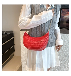 Detailed close-up of red woven crescent bag with gold chain strap on shoulder
