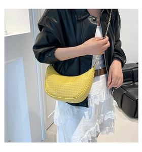 Détail du sac croissant tressé jaune avec chaîne dorée sur une tenue de mannequin