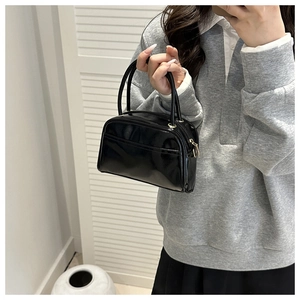 Close-up of black patent leather Boston bag with gold zipper and minimalist front pocket