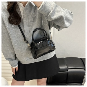 Polished black pillow bag shown on model with adjustable strap and gold hardware detail