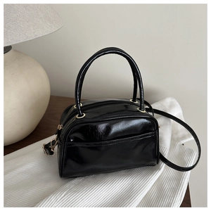 Detailed macro of black glossy Boston bag featuring gold hardware and a front pocket