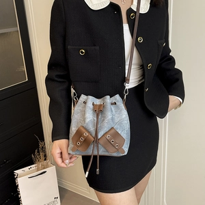 Blue denim drawstring bucket bag with brown leather accents shown as a crossbody wear