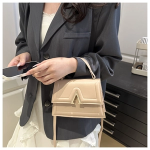 Detail view of a beige matte leather square bag with gold V hardware on a model