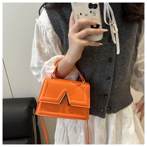 Detail of bright orange handbag featuring stitching and golden V-shaped metal lock