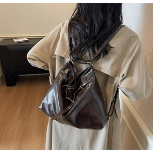 Detail of a dark brown vintage PU leather bucket backpack with drawstring closure on model